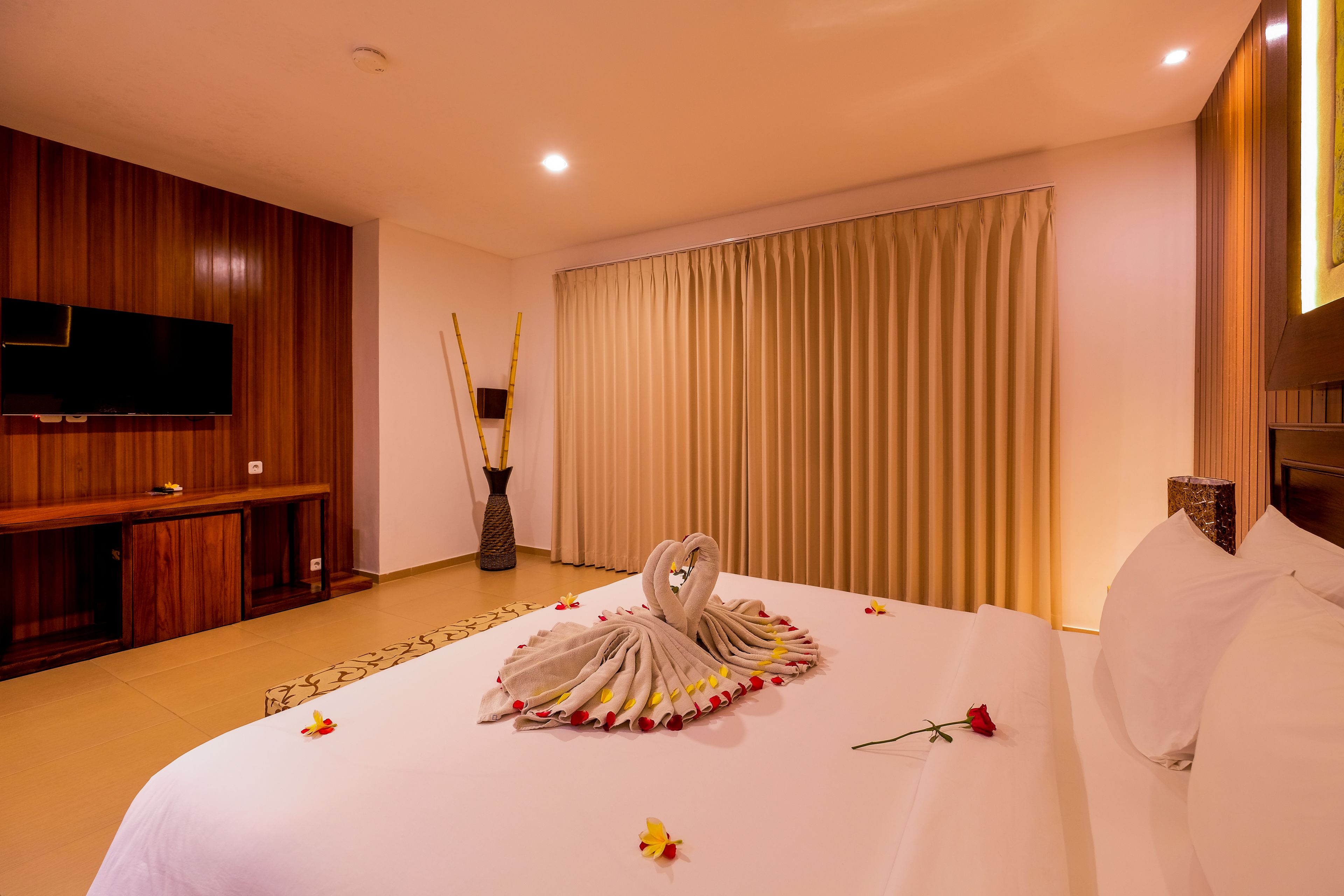 A hotel room with a bed, a TV, a wooden cabinet, and a large window with curtains.