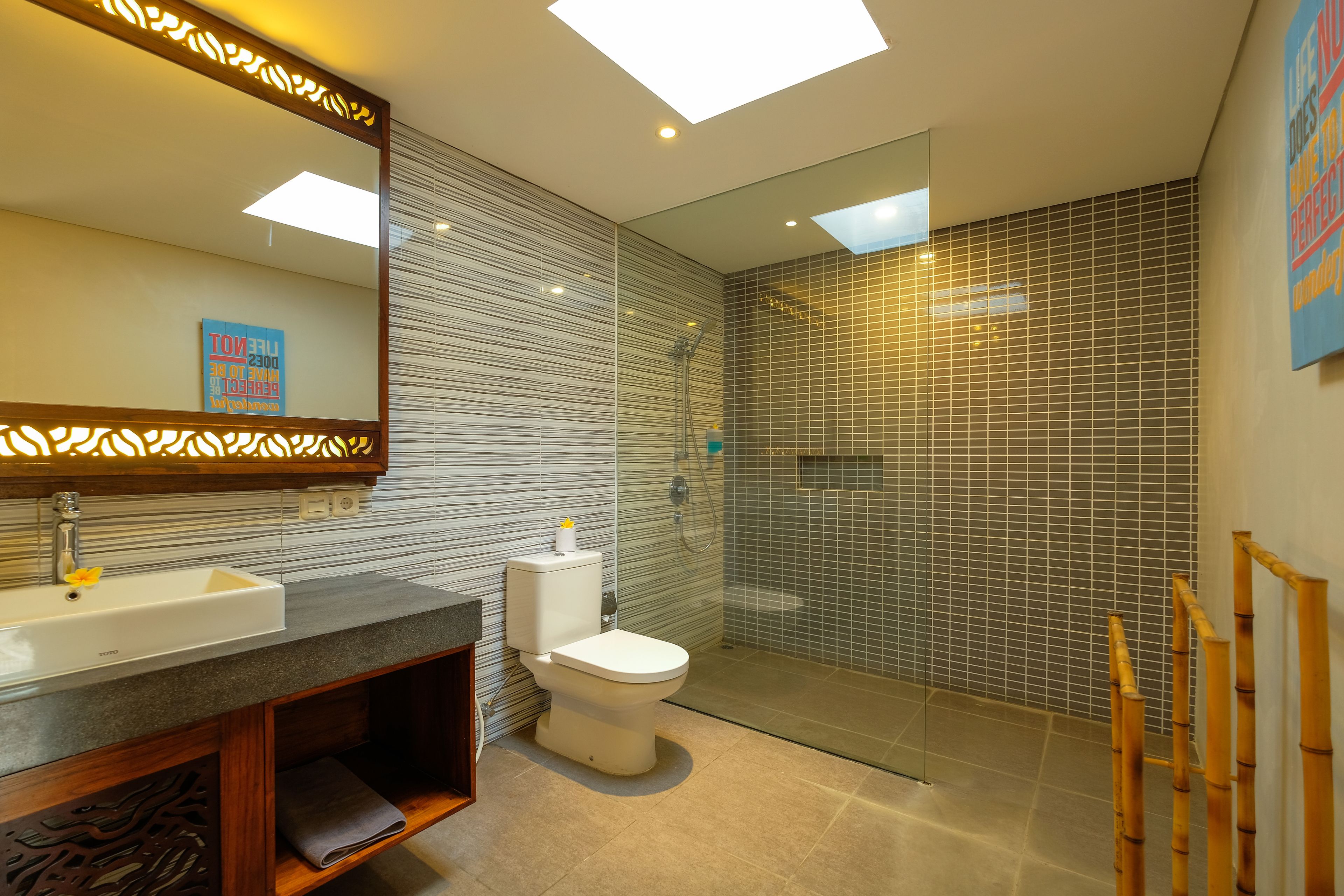 A modern bathroom with a large mirror, a sink, a toilet, and a glass-enclosed shower area.