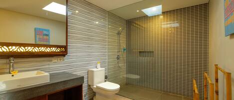 A modern bathroom with a large mirror, a sink, a toilet, and a glass-enclosed shower area.