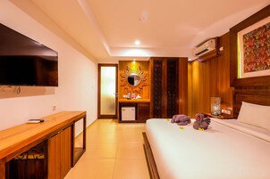 A hotel room with a bed, a desk, a TV, a mirror, and a wall-mounted air conditioner.