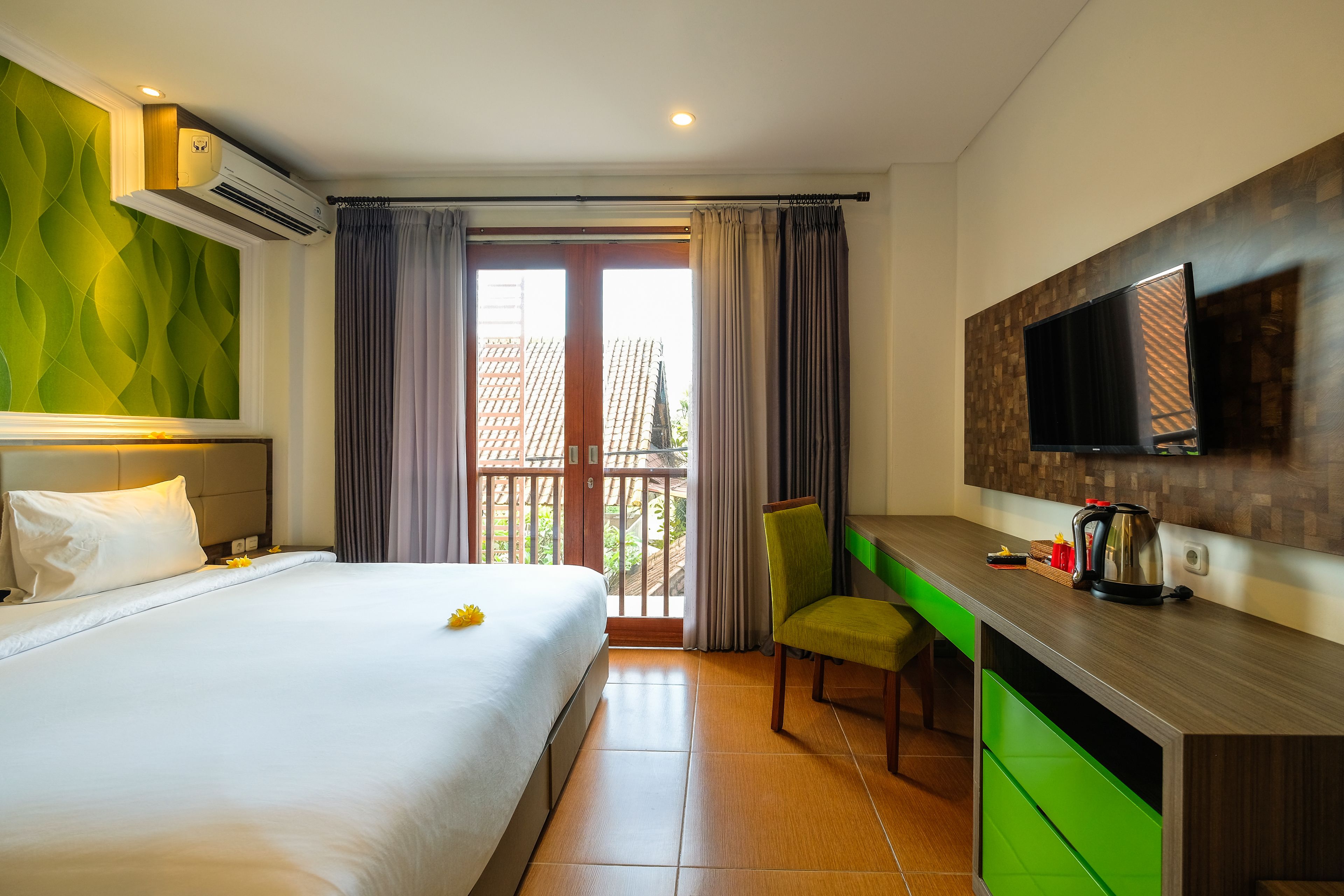 A hotel room with a bed, a desk, a chair, a television, and a balcony with curtains.