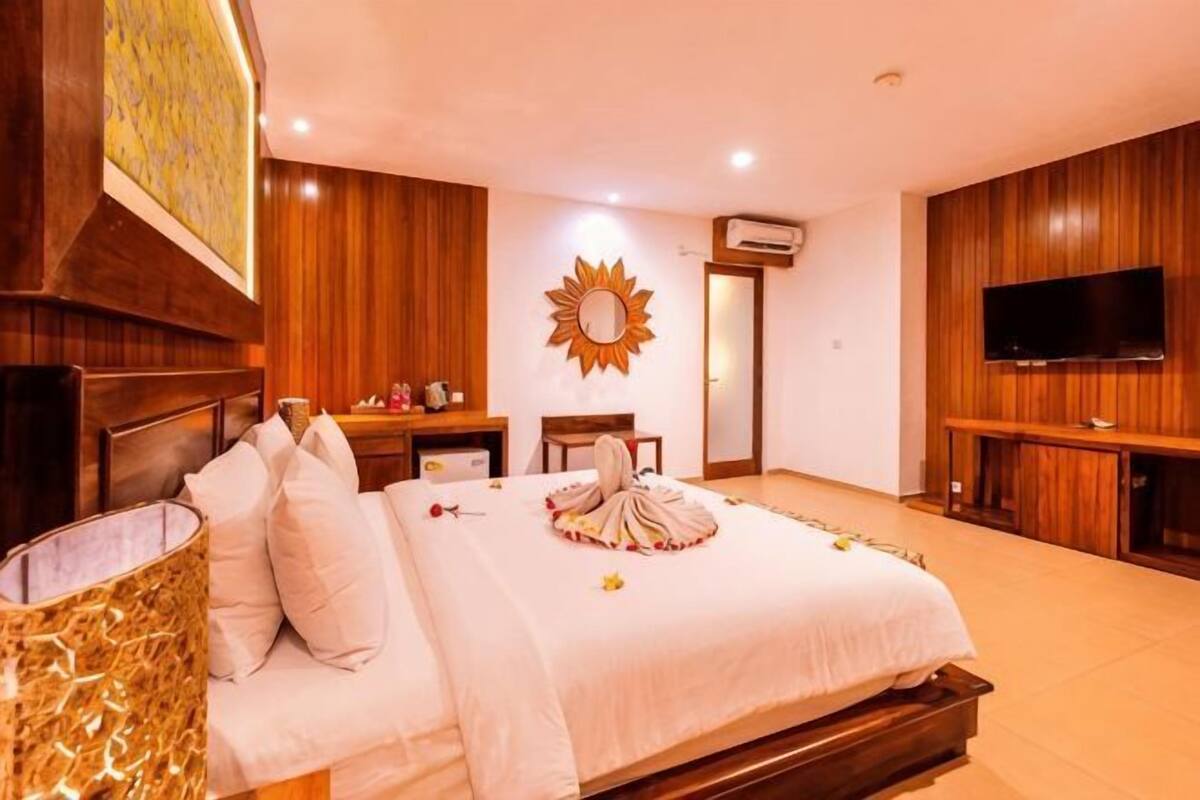Una habitación de hotel con una cama, un televisor, un espejo con forma de sol y un panel de pared de madera.