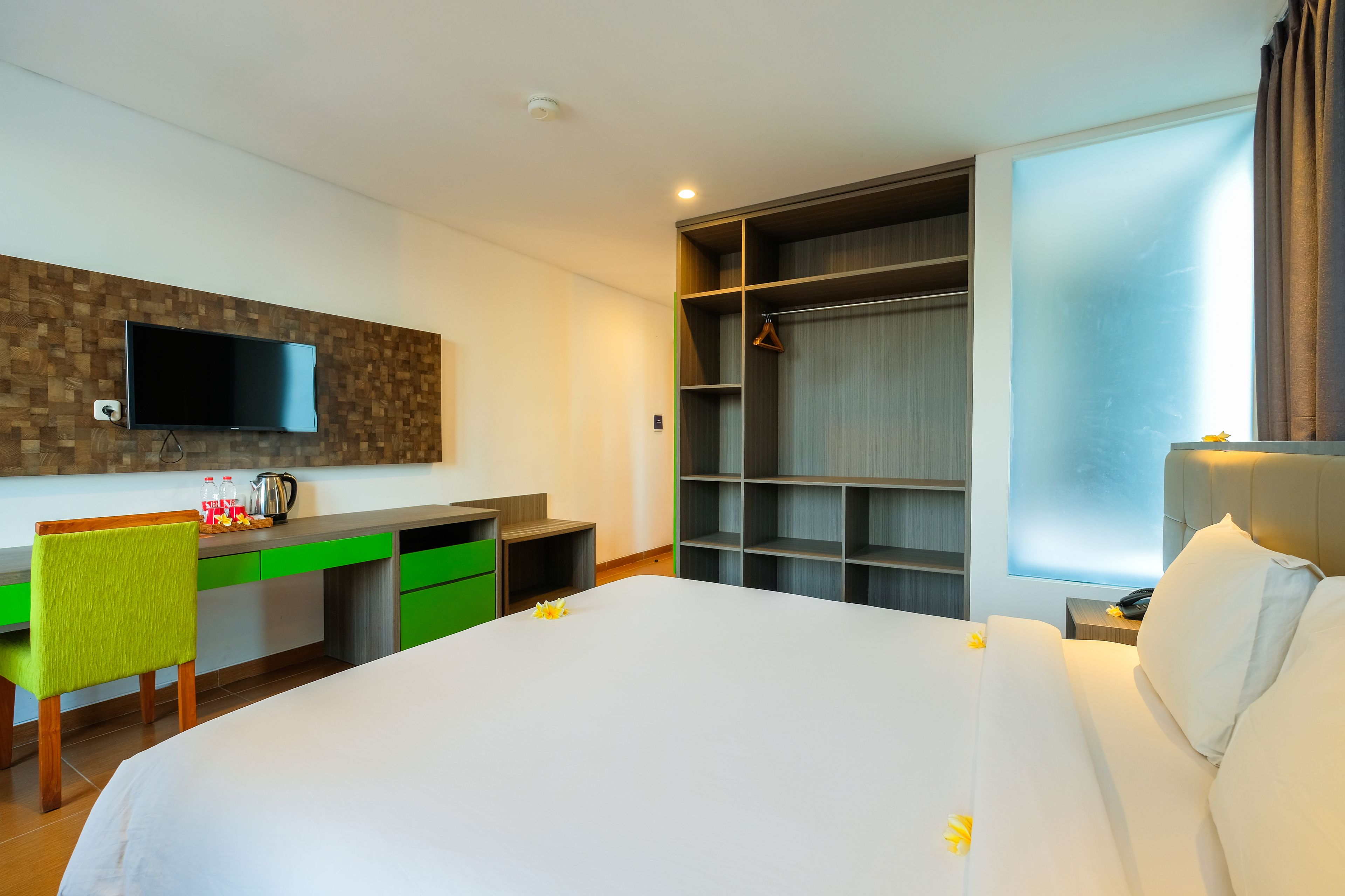 Habitación de hotel con una cama grande, un escritorio con silla, un televisor montado en una pared de madera y un armario con espejo.
