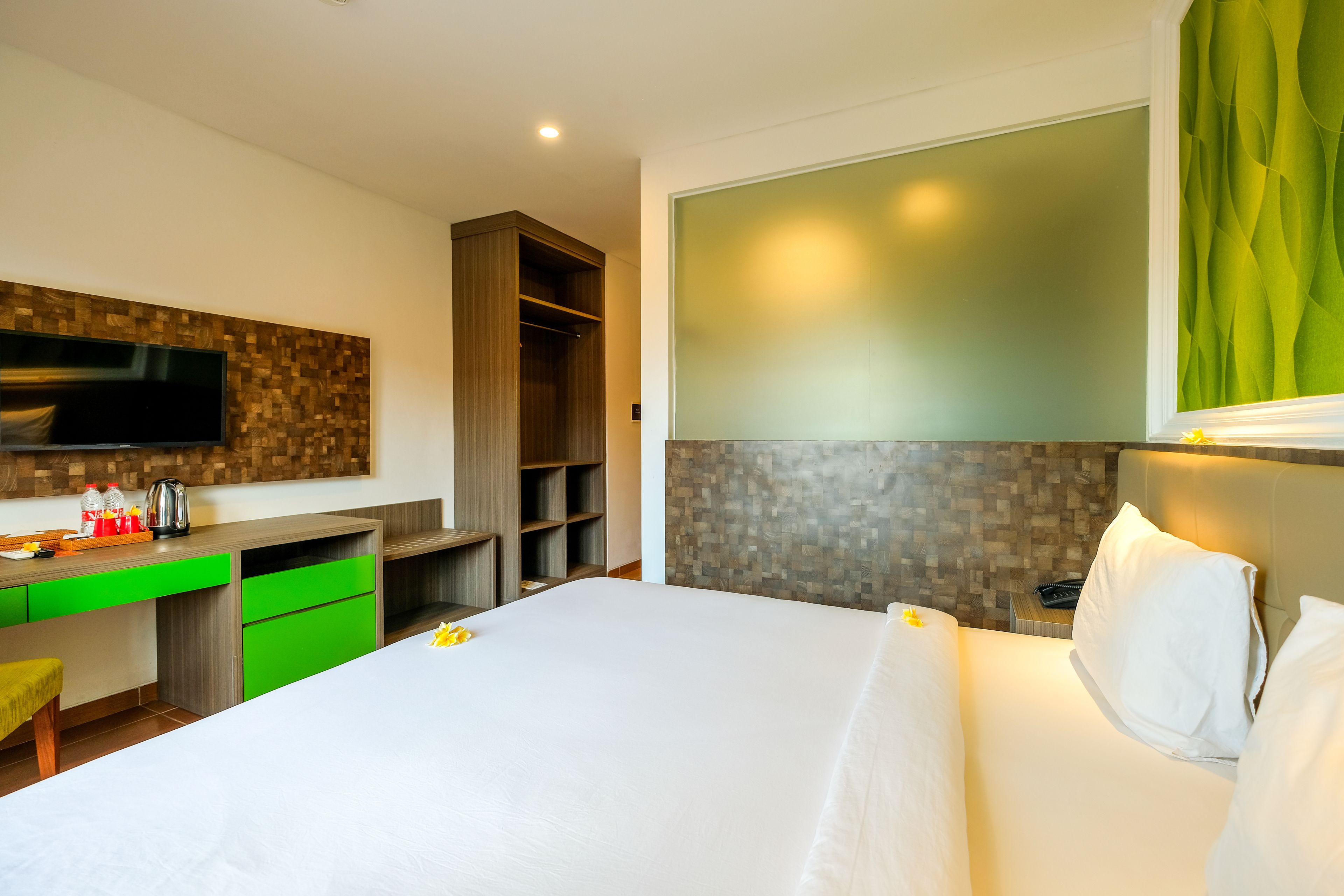 A hotel room with a bed, a desk with green drawers, a wardrobe, a television, and a green curtain.