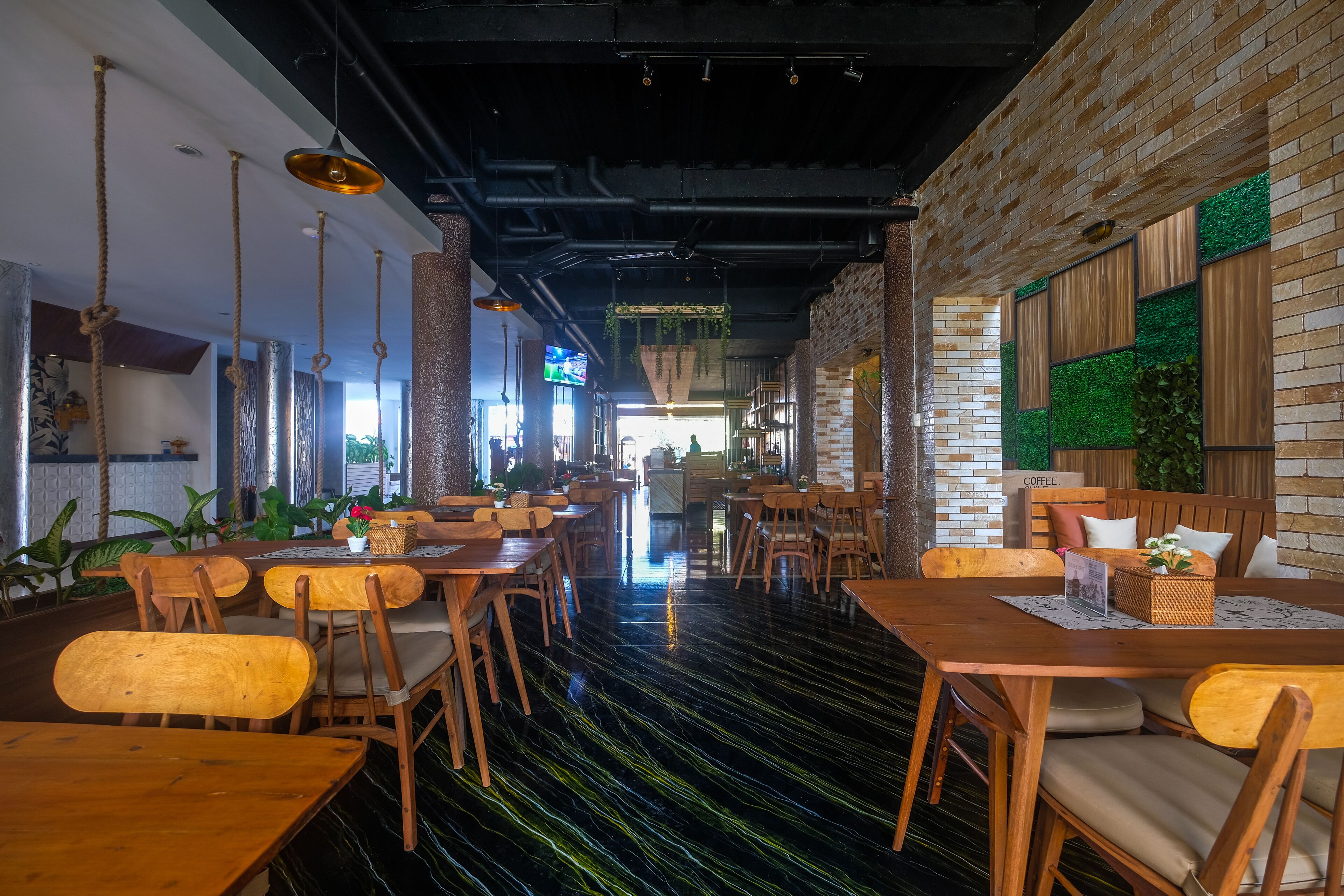 A restaurant with wooden tables and chairs, a black and green floor, and brick walls.