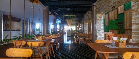 A restaurant with wooden tables and chairs, a black and green floor, and brick walls.
