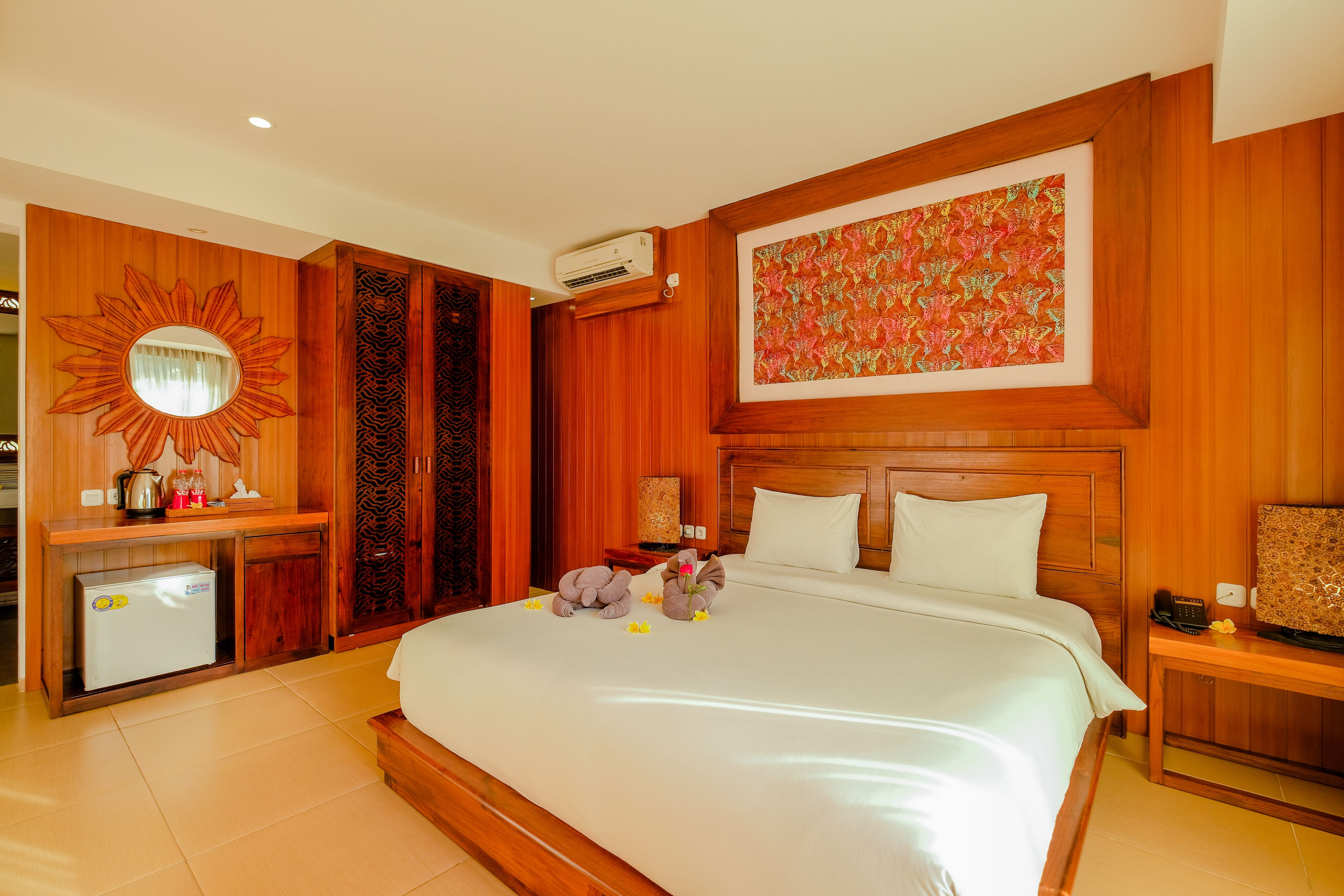 A hotel room with a large bed, wooden paneling, a decorative mirror, a small refrigerator, and a wall-mounted air conditioner.
