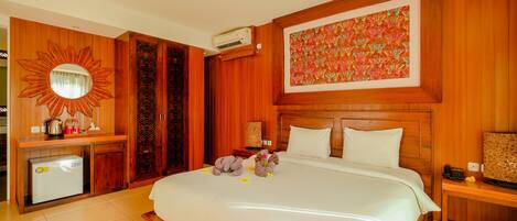 A hotel room with a large bed, wooden paneling, a decorative mirror, a small refrigerator, and a wall-mounted air conditioner.