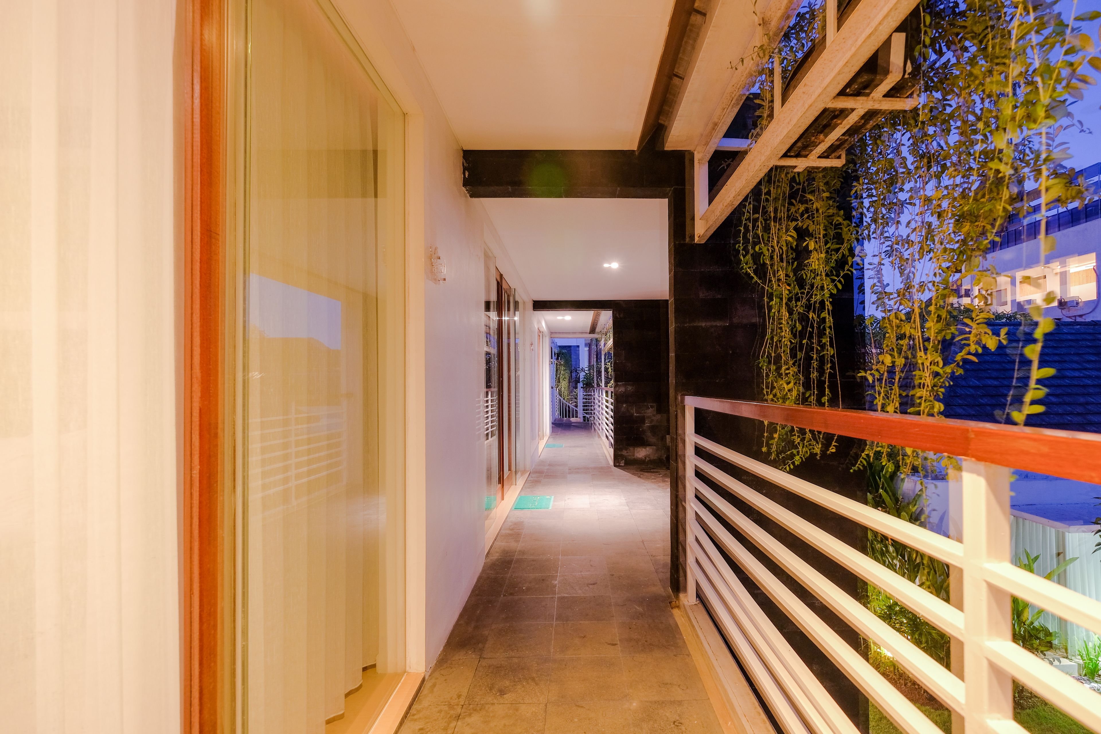 A corridor with glass doors, a wooden railing, and a view of a building with plants.