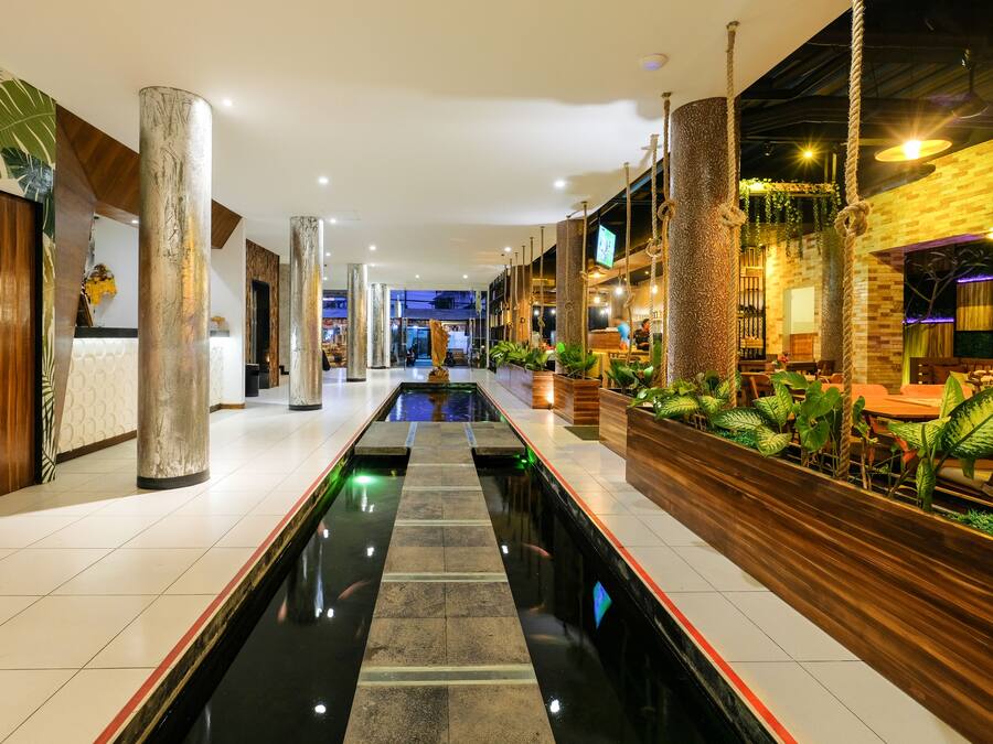 Un vestíbulo de hotel con una fuente central, columnas de madera y una zona de estar con plantas.