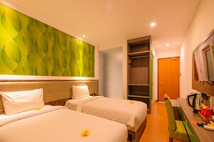 Habitación de hotel con dos camas, una pared verde, un escritorio de madera y una cafetera.