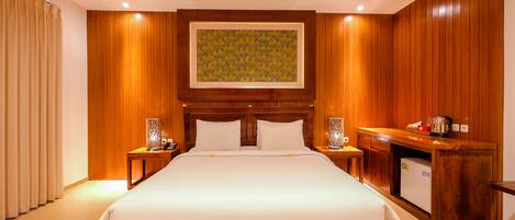 A hotel room with a large bed, wooden paneling, a small kitchenette, and a painting above the bed.