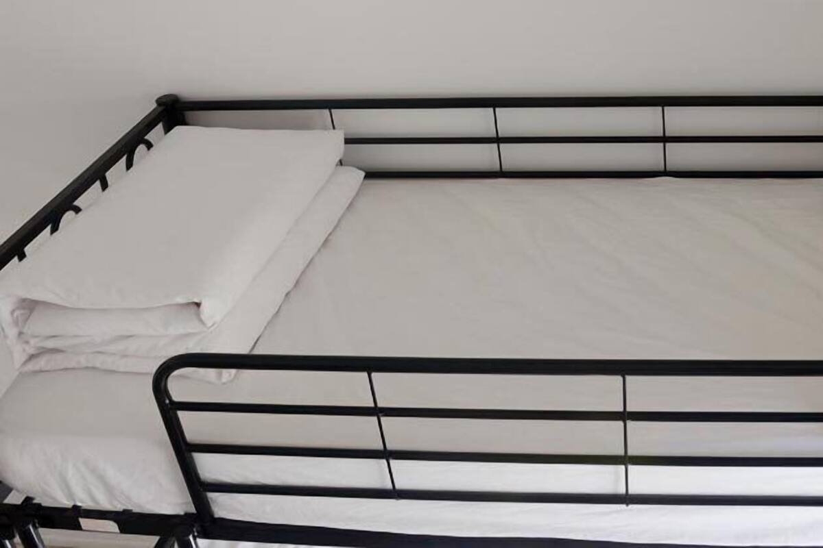 A single bed with a black metal frame, white bedding, and a plain wall in the background.