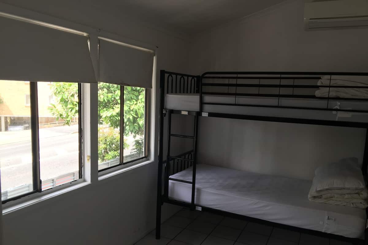 A bunk bed room with a window, white walls, and a tiled floor.