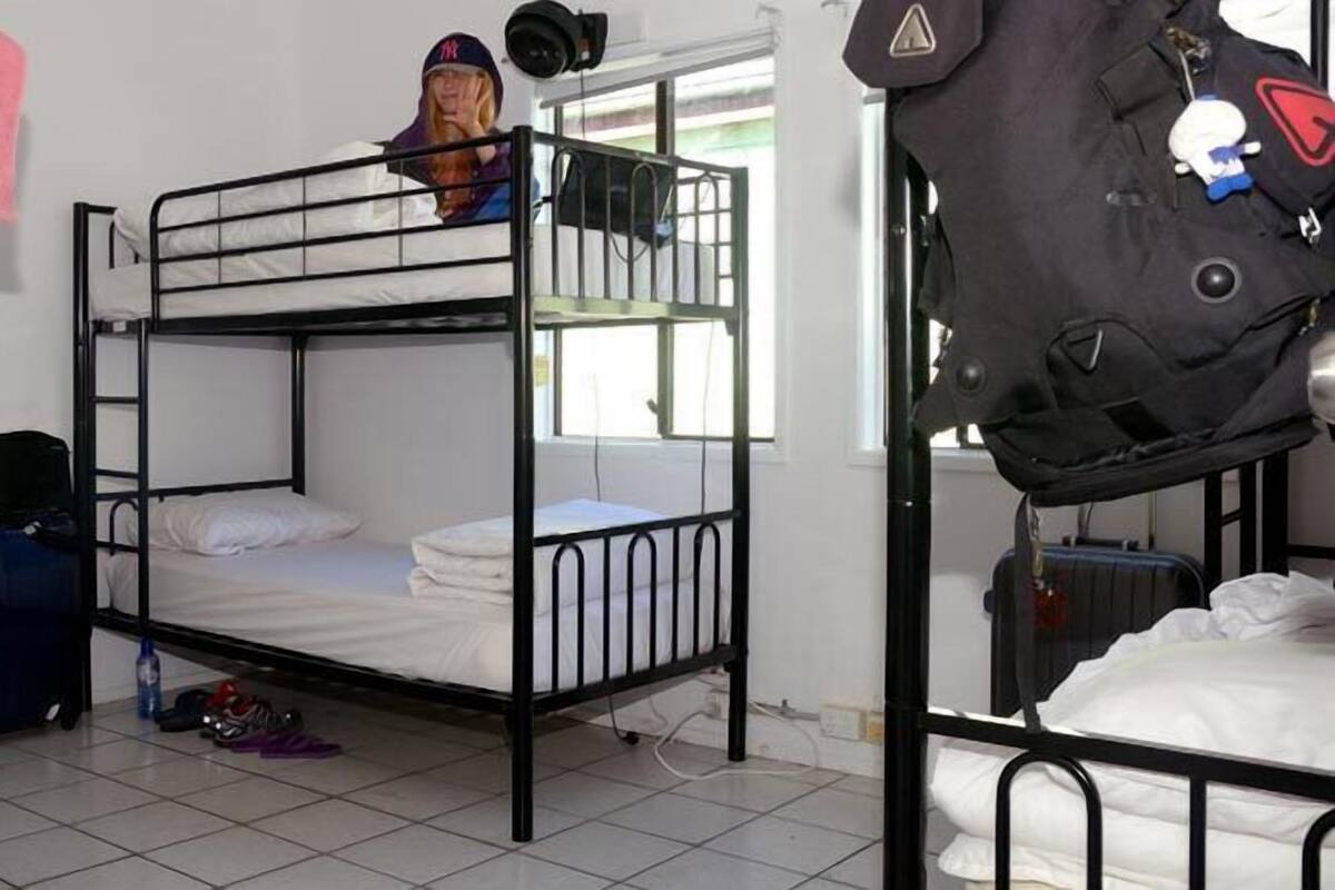 A dormitory room with bunk beds, a suitcase, and a bed with a pink towel.
