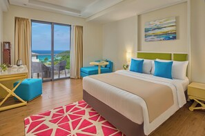 Habitación de hotel con una cama grande, un escritorio con silla, una mesita y vista al océano.