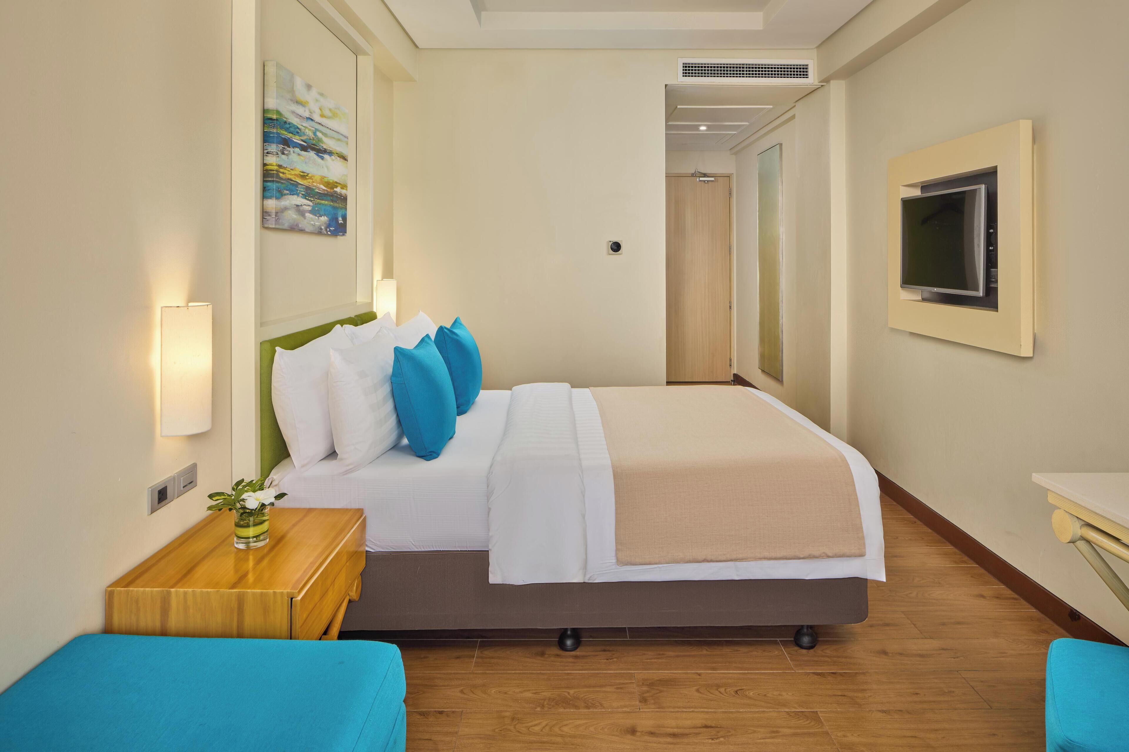 Una habitación de hotel con cama, mesita de noche, televisión y un cuadro en la pared.