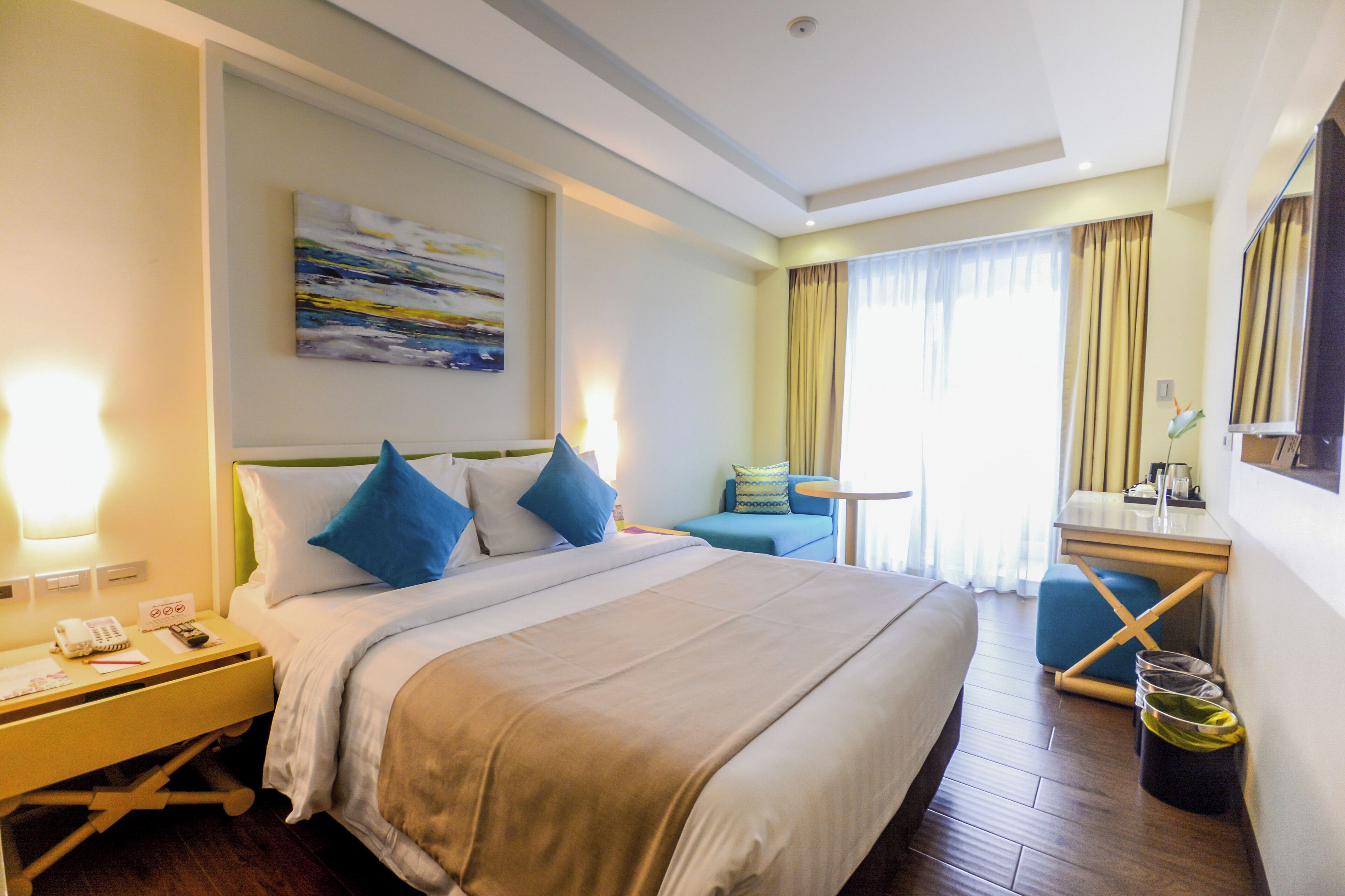 A hotel room with a bed, bedside table, lamp, and a desk with a chair.