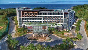 A modern hotel with a rooftop terrace, multiple floors, and a view of the ocean.
