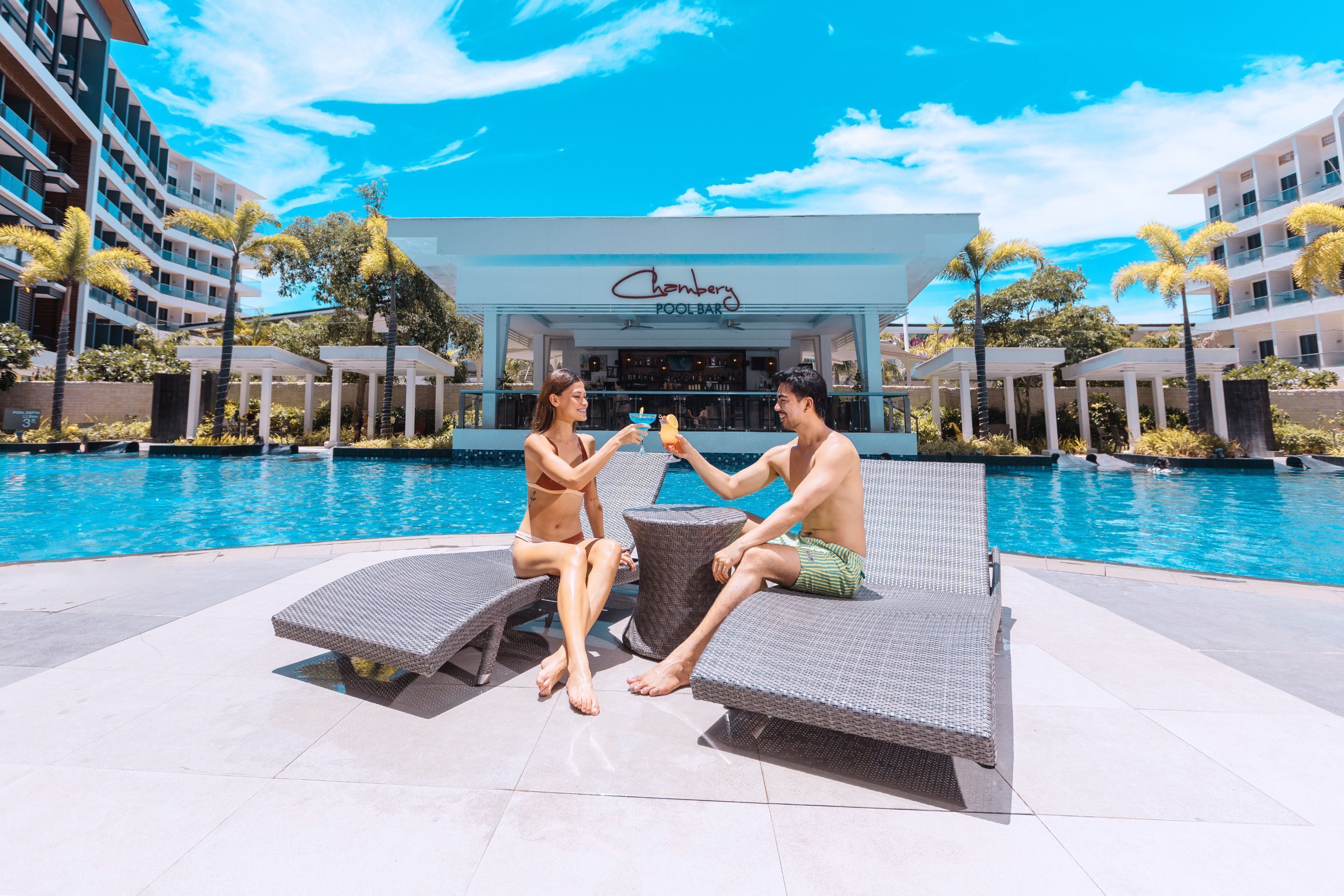 A poolside area with lounge chairs and a pool. A building with a sign reading "Chamber Pool Bar" is visible in the background.