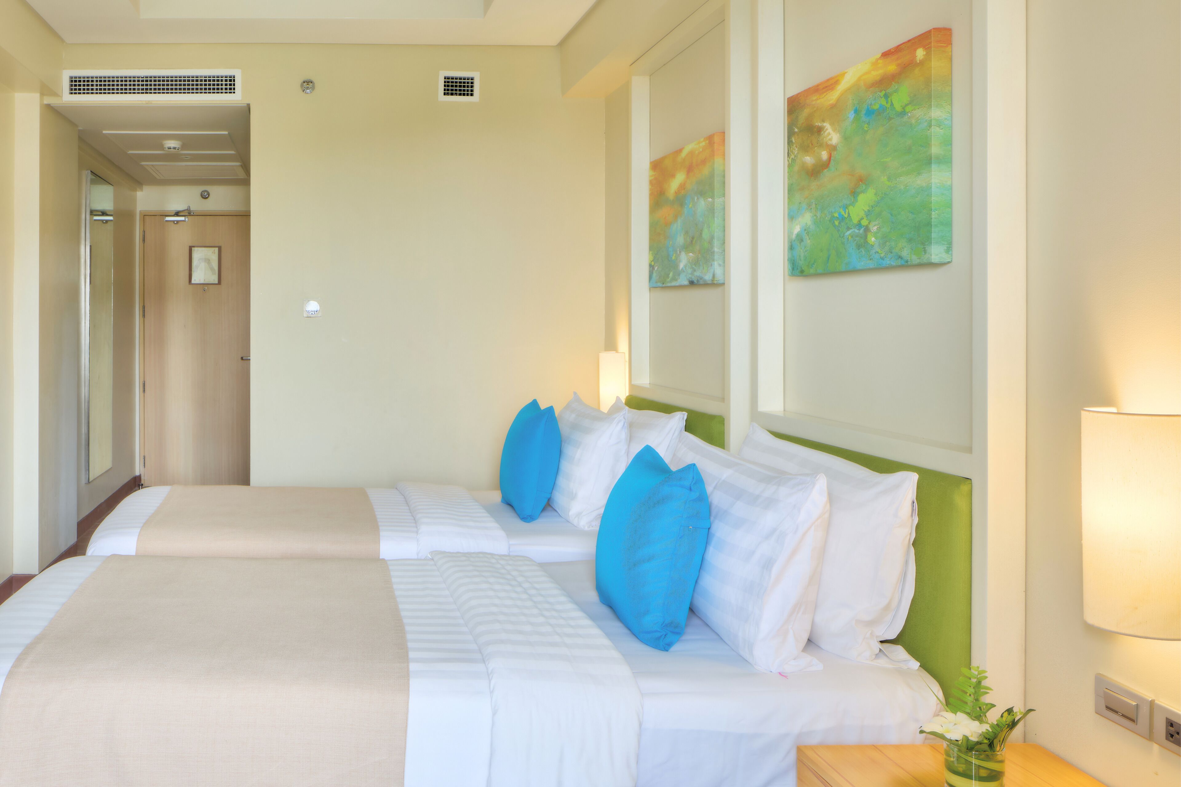 A hotel room with two beds, a green headboard, and a painting on the wall.