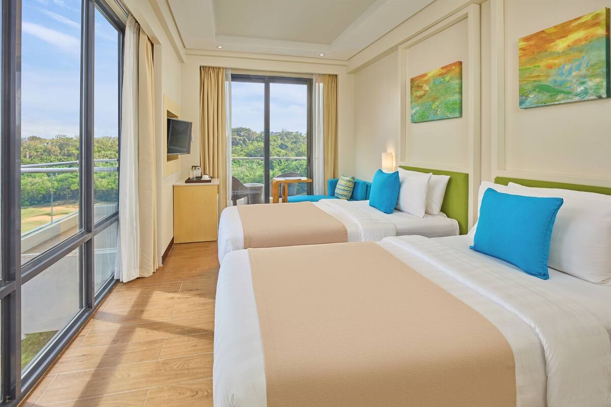A hotel room with two beds, a TV, and a balcony with a view of greenery.