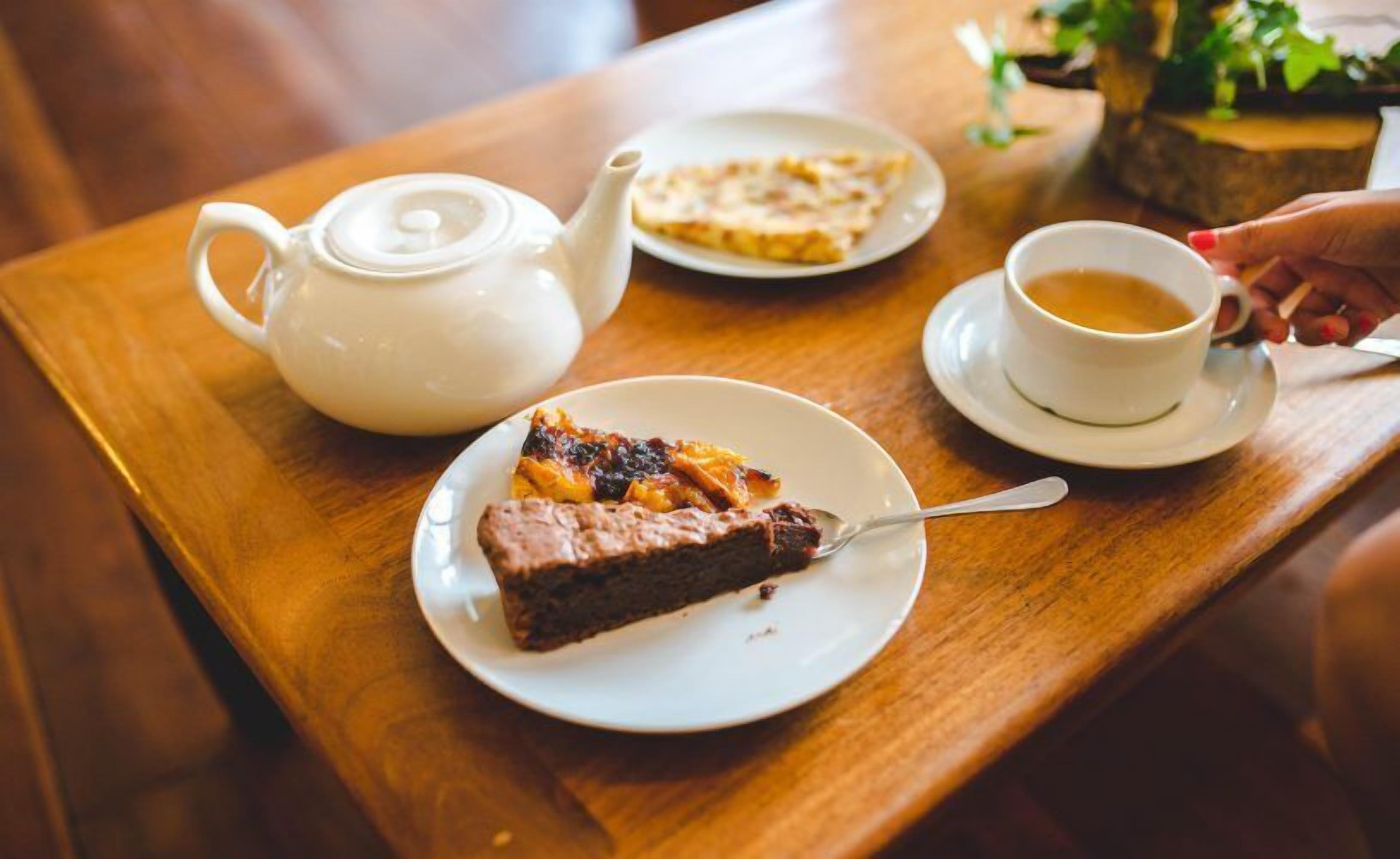 A wooden table with a teapot, a plate with a slice of pie, and a cup of tea.