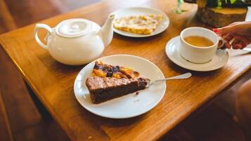 A wooden table with a teapot, a plate with a slice of pie, and a cup of tea.