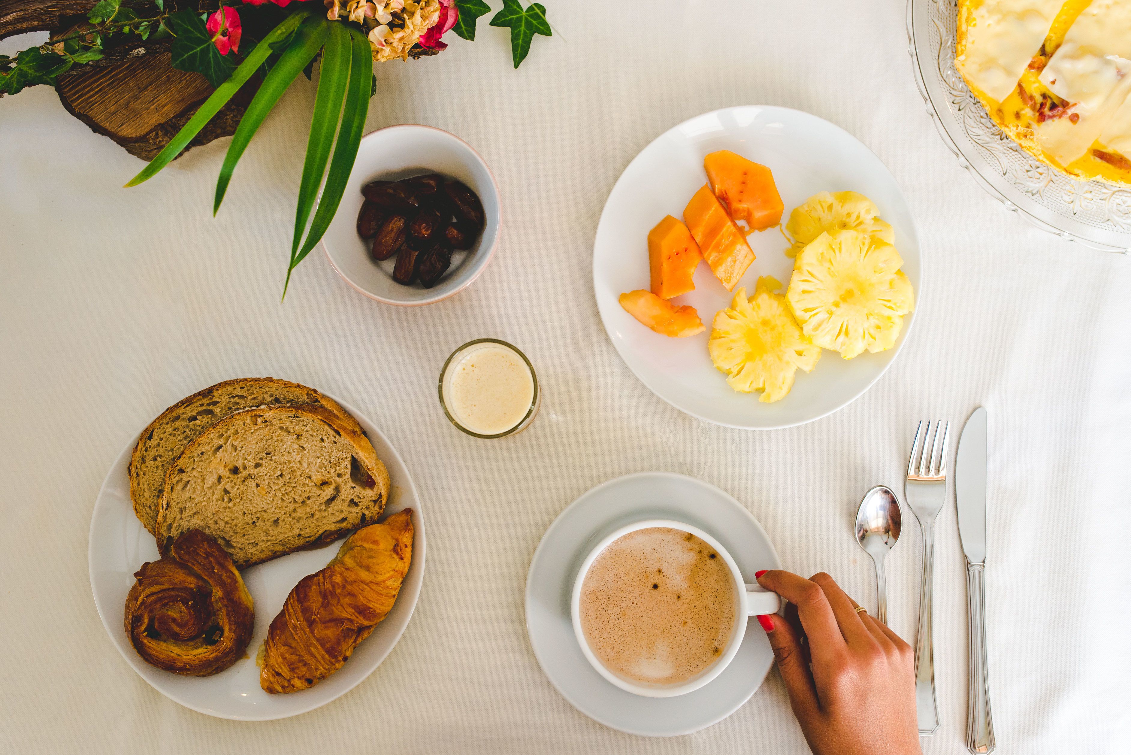 Una mesa con pan, bollería, fruta y una taza de café para el desayuno.