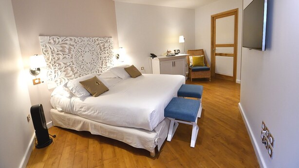 A bedroom with a large bed, bedside lamps, a wicker chair, a desk, and a television on the wall. - Le Tsilaosa Hotel & Spa (Cilaos)