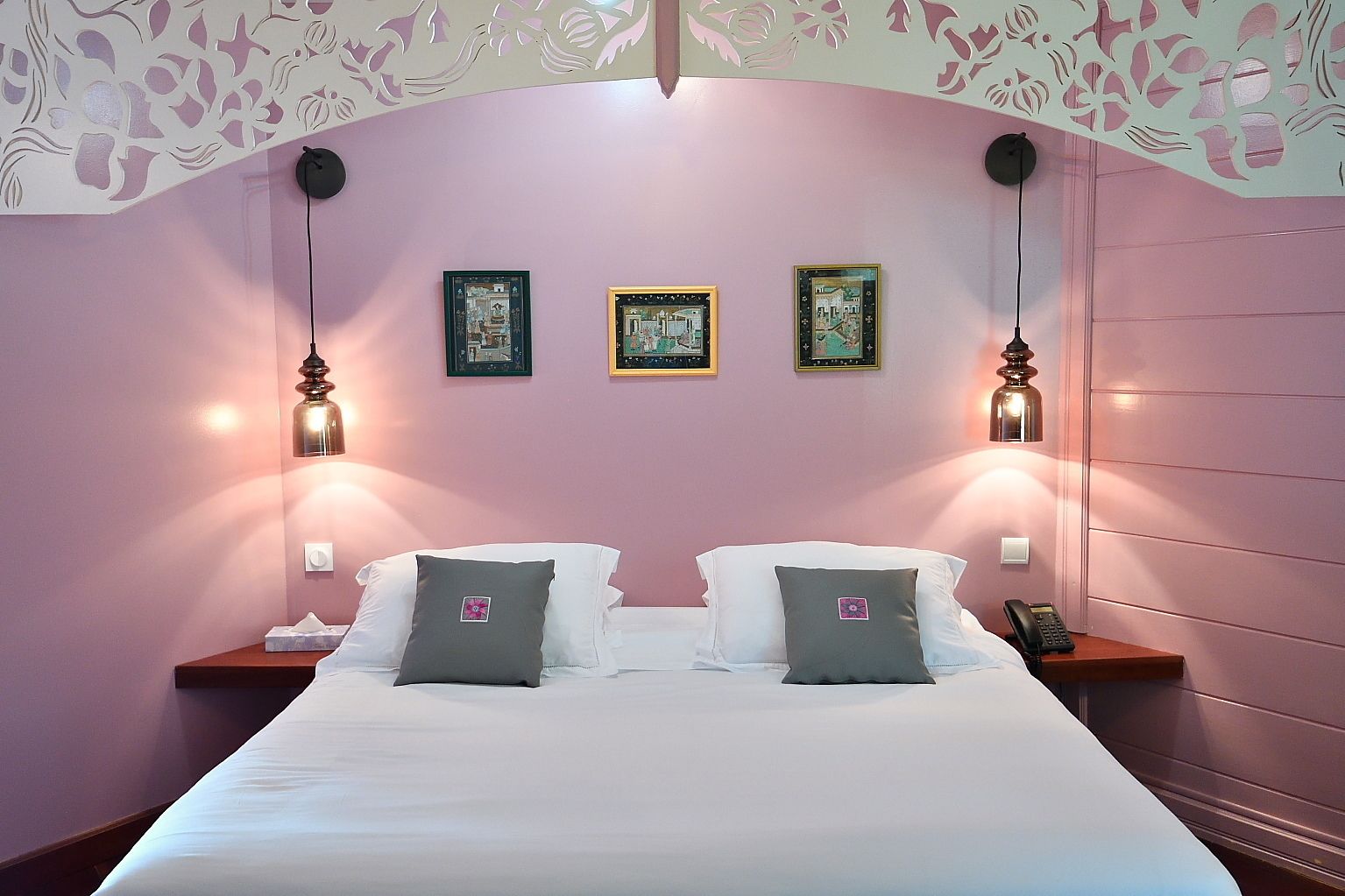 Ein Hotelzimmer mit einem Bett, zwei Nachttischen und drei gerahmten Bildern an der Wand.