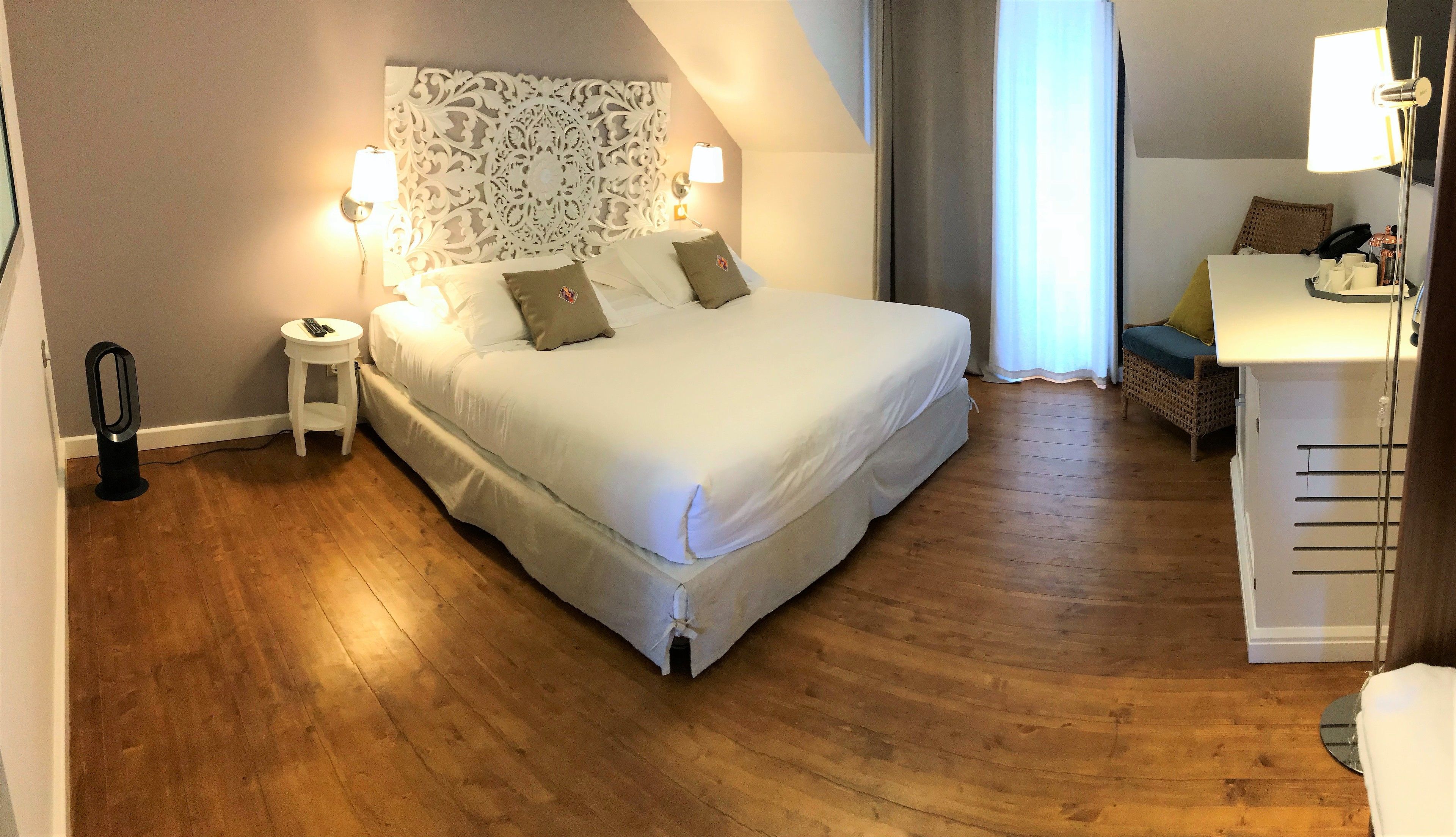 A neatly arranged bedroom with a large bed, bedside lamps, a small table, and a decorative headboard.