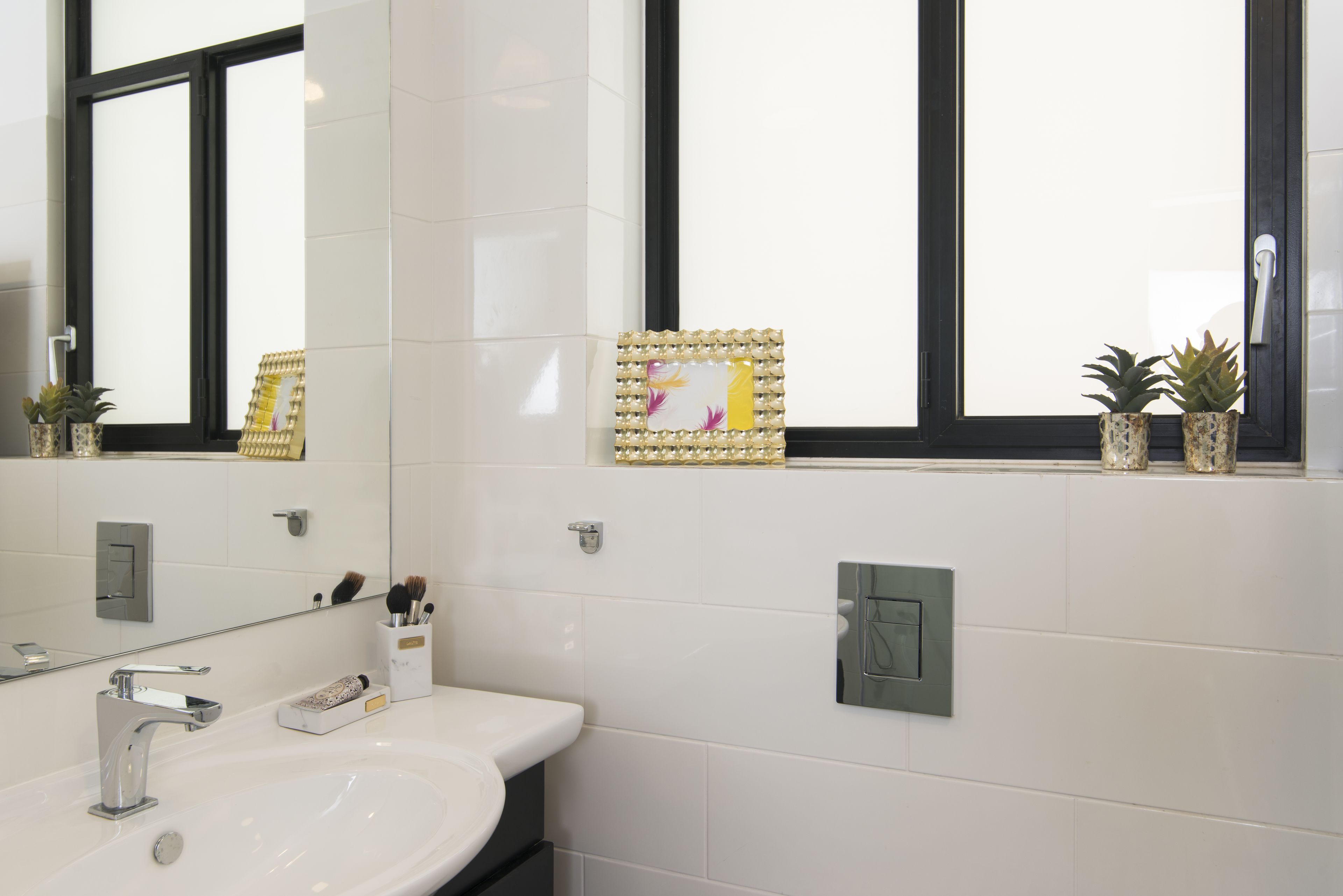 A bathroom with a white sink, a mirror, and a window with decorative tiles.