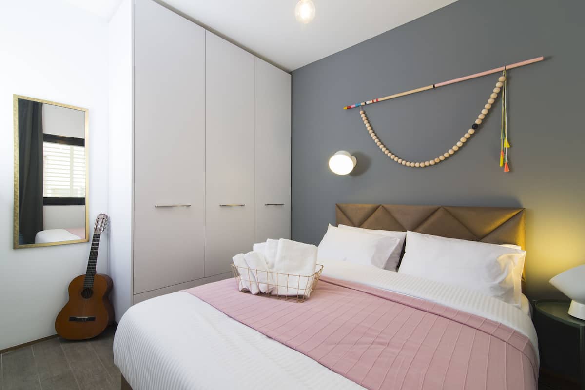 A bedroom with a bed, a guitar, a wall-mounted bead curtain, and a bedside lamp.