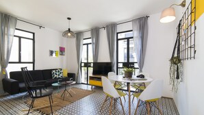 A modern living room with a black sofa, a dining table with chairs, a TV, and a patterned floor. - Mr. Brooklyn - By TLV2GO (Tel Aviv)