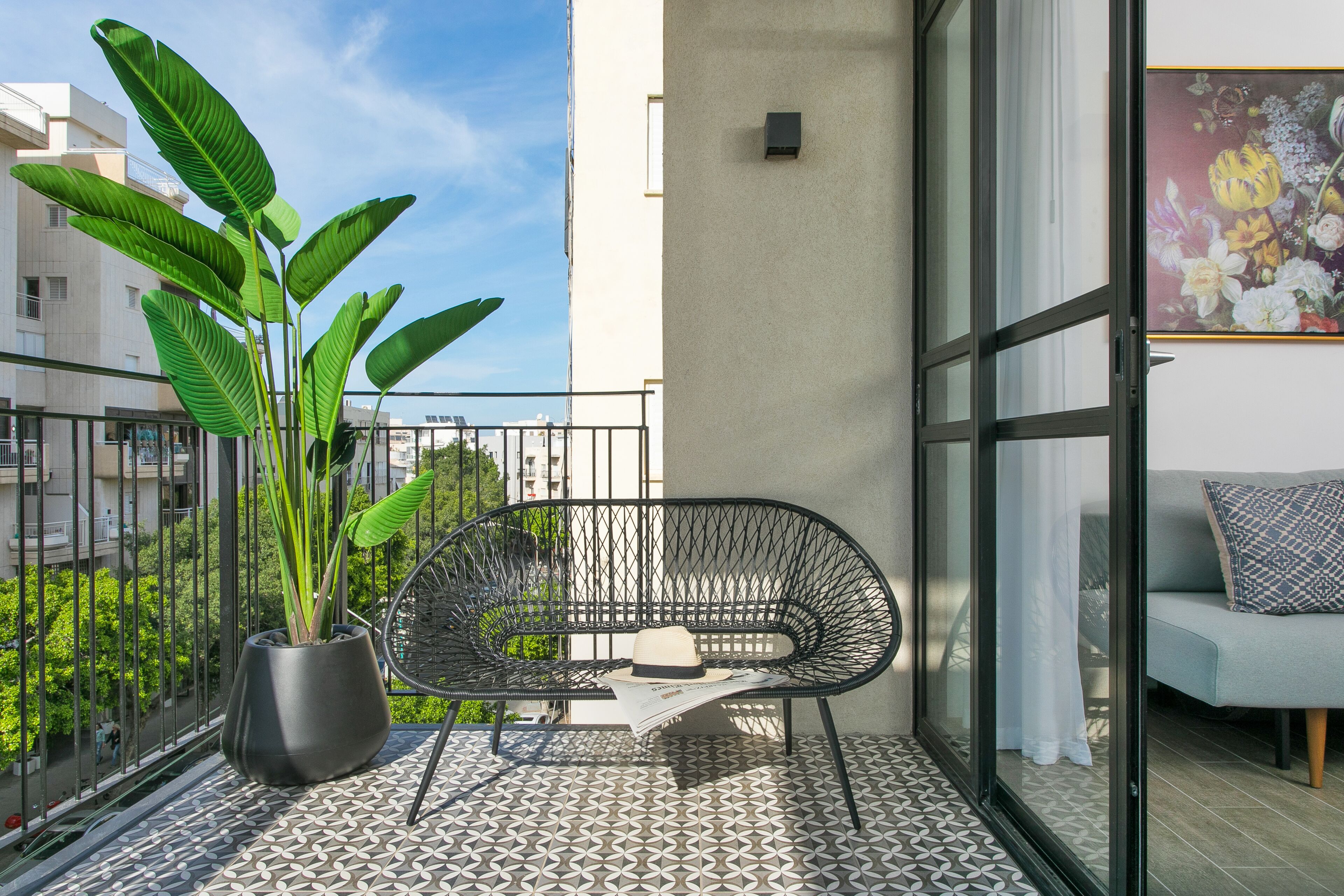 Ein Balkon mit schwarzem Metallstuhl, einem Blumentopf und einem gemusterten Boden.