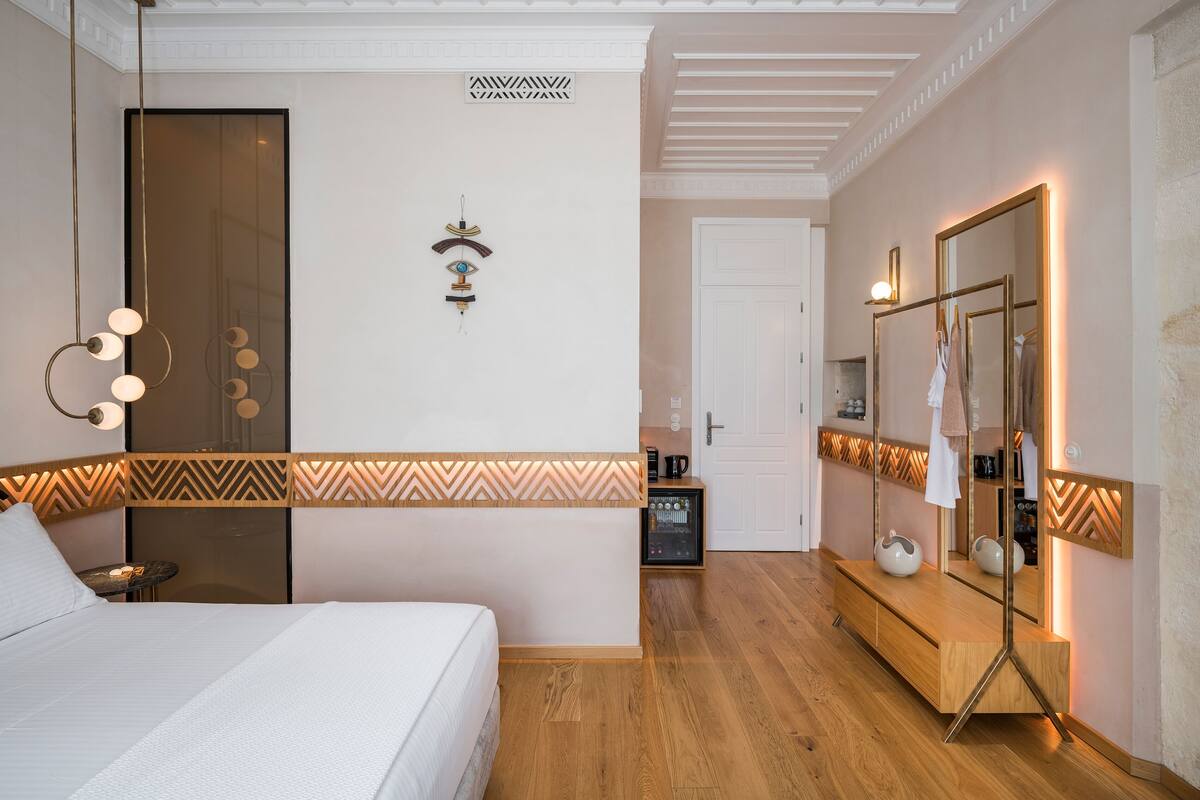 A modern hotel room with a large bed, a vanity with a mirror, and a small table with a lamp.