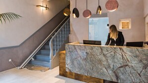 Un comptoir d’accueil avec un plateau en marbre, un escalier et des luminaires suspendus.