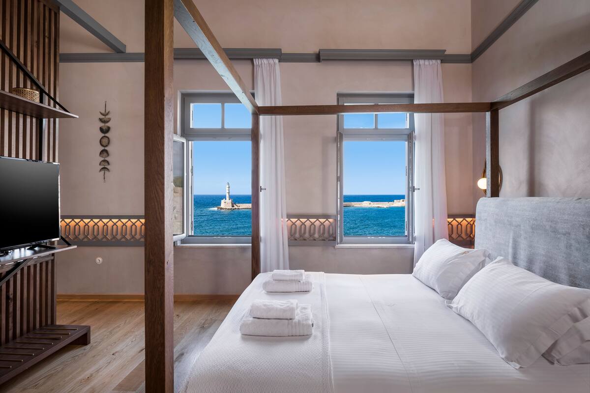 A bedroom with a large bed, a TV, and a view of the sea.