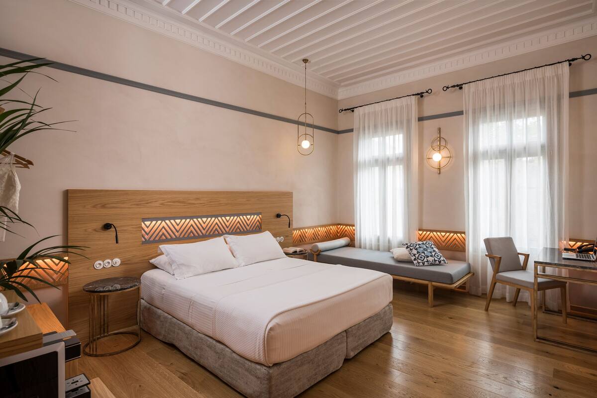 A modern bedroom with a large bed, bedside tables, a desk, and a seating area.