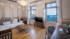 Un salon moderne comprenant un canapé, une table basse, un téléviseur et un bureau avec un ordinateur portable. De grandes fenêtres offrent une vue sur la mer et un phare.