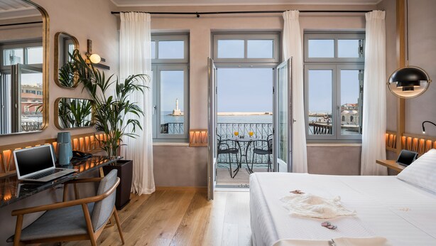 Une chambre d’hôtel avec un lit, un bureau avec un ordinateur portable, une plante en pot et un balcon offrant une vue sur la ville.