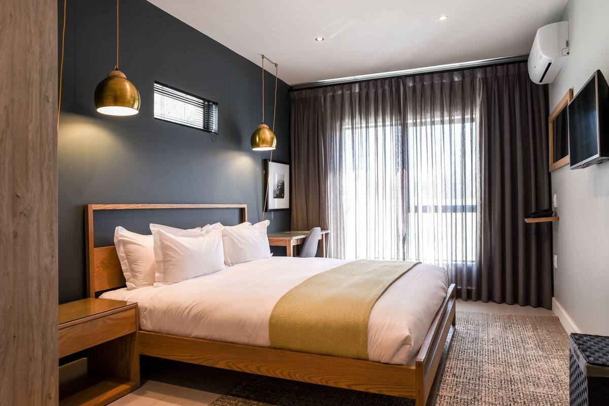 Et moderne hotelværelse med en træseng, et skrivebord og et stort vindue med gardiner.