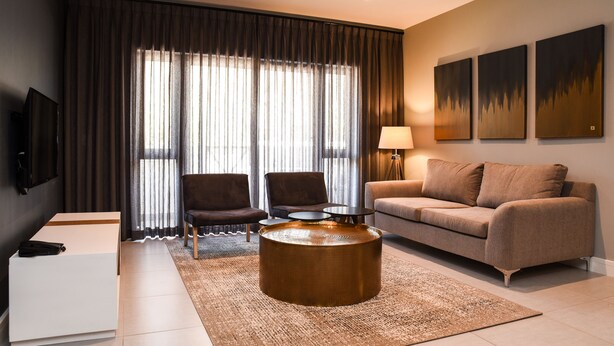 Una sala de estar moderna con un sofá, dos sillones, una mesita de centro, un televisor y obras de arte en la pared.