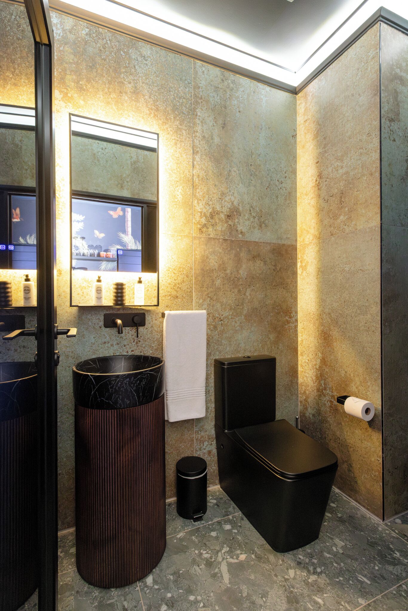 A modern bathroom with a marble sink, a large mirror, a black trash bin, and a toilet.