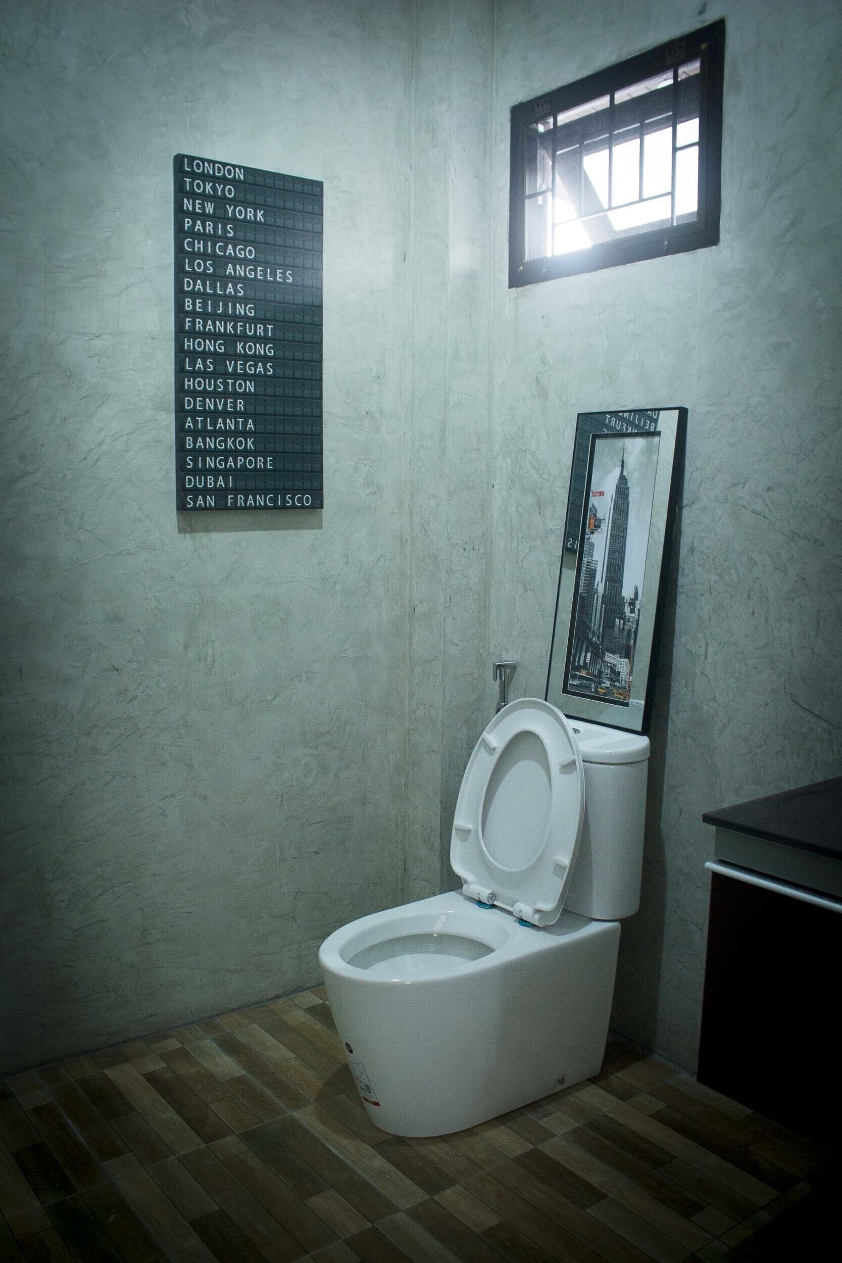 A bathroom with a white toilet, a list of city names on the wall, and a framed picture of a building.
