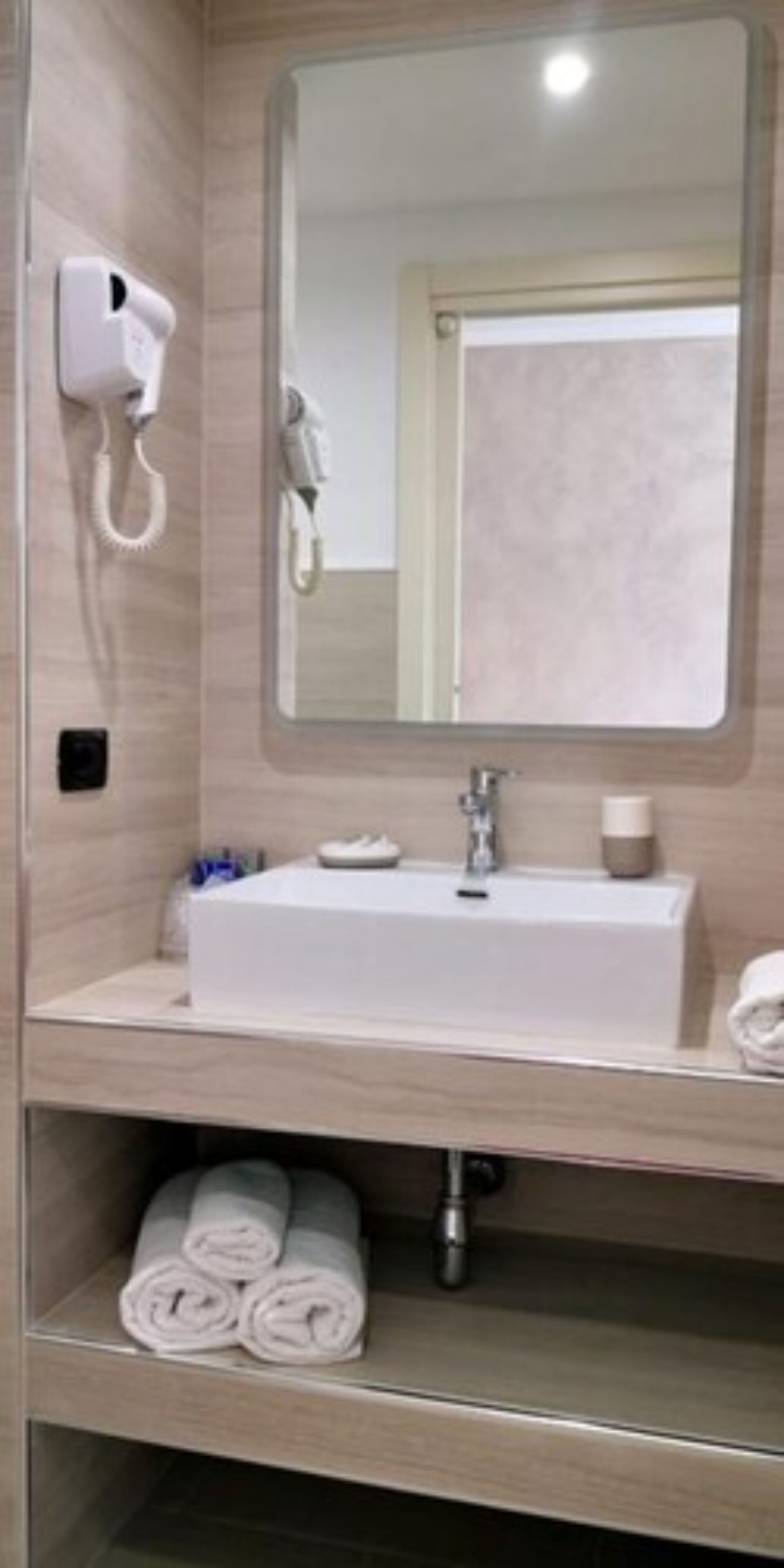 Un baño con lavamanos blanco, espejo, secador de pelo y toallero.