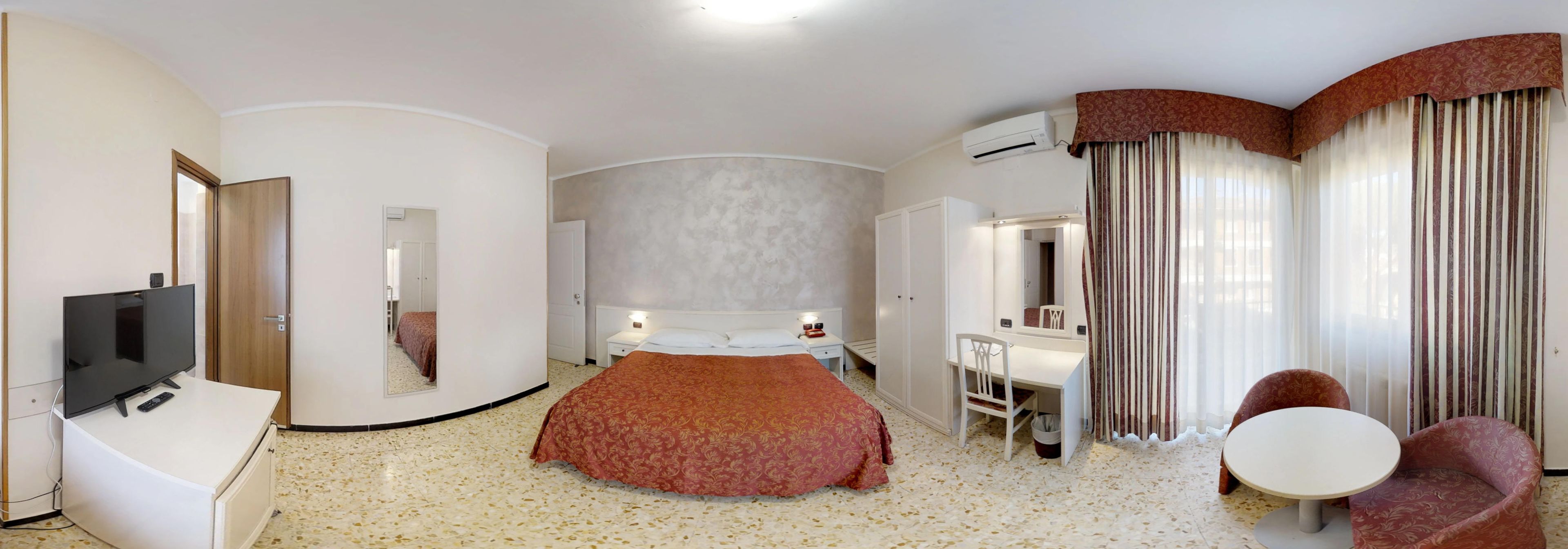A hotel room with a bed, a desk, a chair, a TV, and a bathroom.