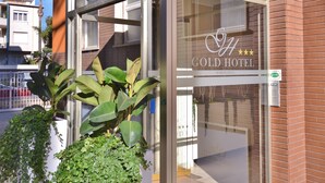 The exterior of a hotel with a glass entrance, large potted plants, and a sign reading "Gold Hotel".