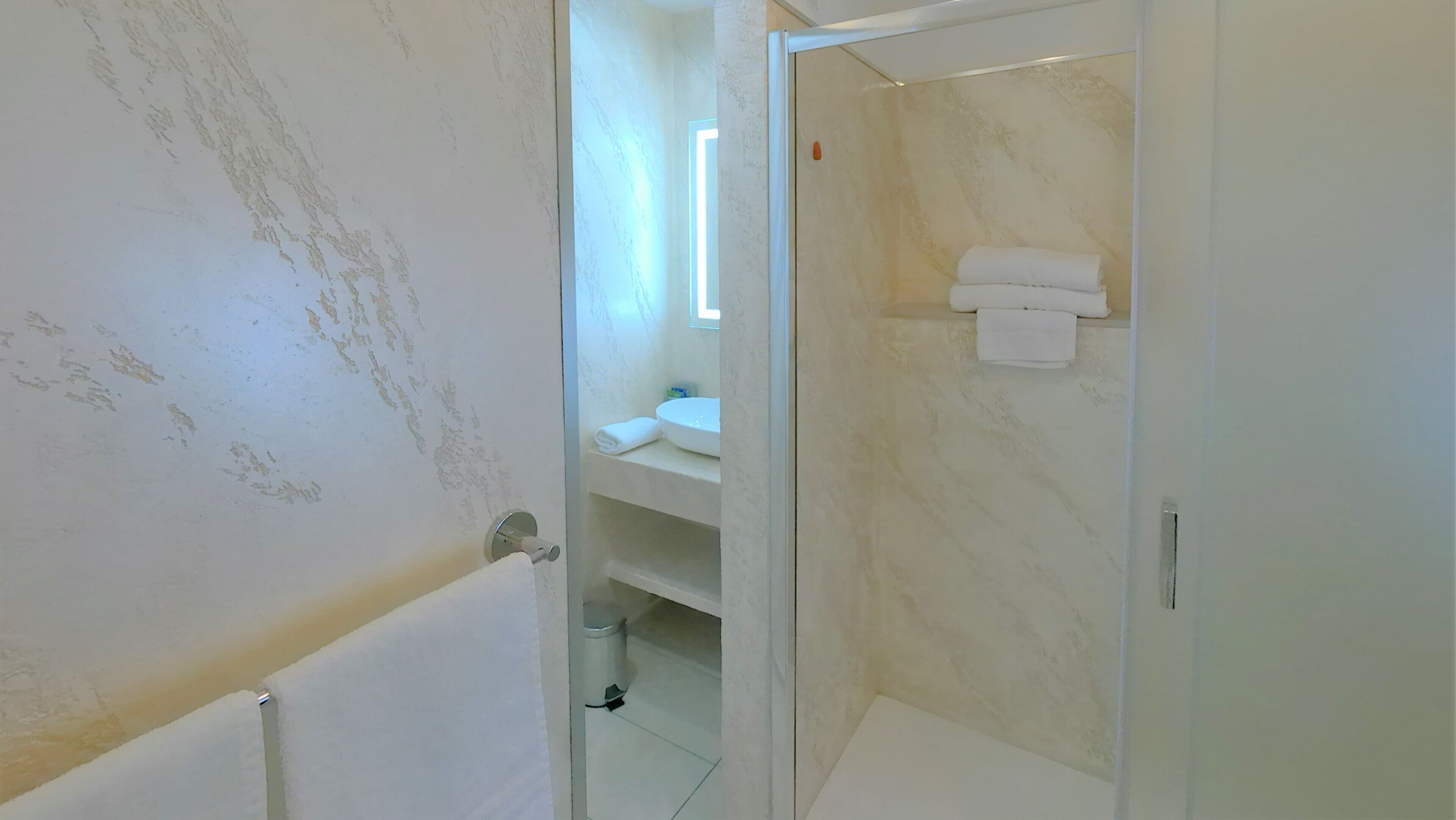 Un baño con lavamanos blanco, espejo y toallero.
